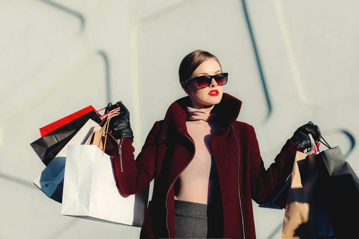 Mujer con abrigo bordó y bolsas de compra.